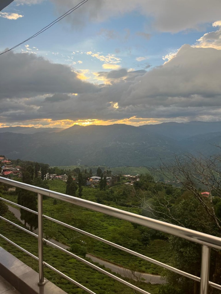 Golden sunrise rays breaking through clouds over lush Kurseong tea gardens